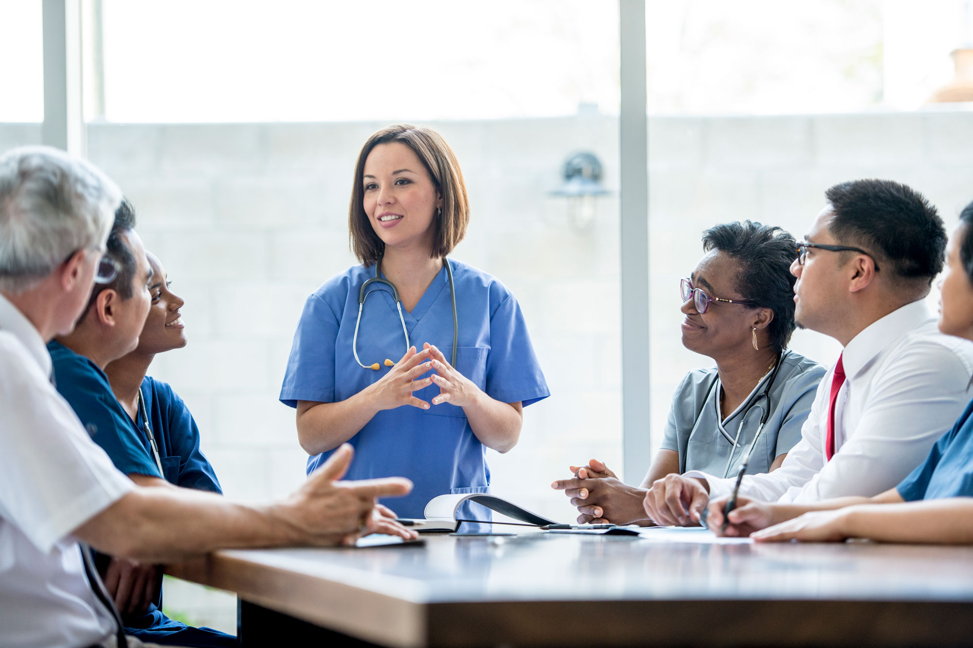 Young female doctor speaks to coworkers around a table